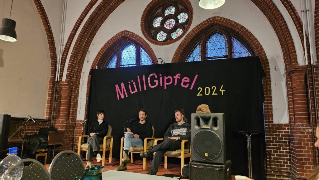 Teilnehmer des Müllgipfels sitzen auf dem Podium